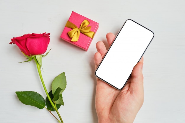 La main tient le téléphone avec copie espace à côté de la boîte-cadeau et le fond rose rouge