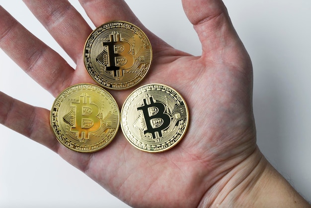 La main tient trois bitcoins sur fond blanc