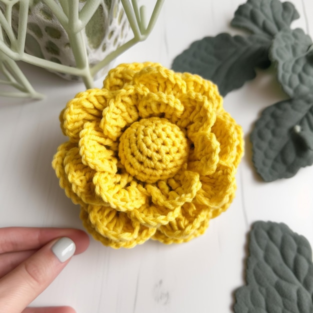 Une main touche une fleur au crochet jaune avec une feuille verte sur le côté.