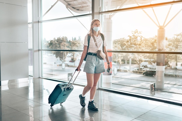 Main de touriste aux cheveux blonds tenant un passeport avec la zone d'attente des bagages de la valise du terminal de l'aéroport pour un voyage. Voyager après la pandémie de Covid-19