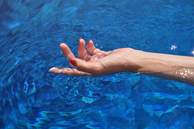 Main d'une touriste féminine méconnaissable nageant dans l'eau propre de la piscine pendant les vacances d'été dans un hôtel tropical