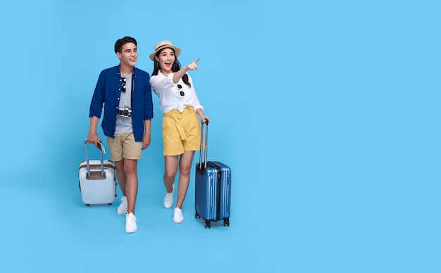 Main de touriste heureux couple asiatique pointant vers l'espace de copie avec des bagages allant voyager en vacances isolé sur bleu.