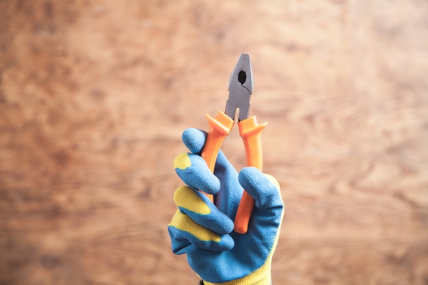 Main de travailleur tenant une pince sur un mur en bois