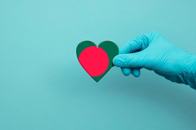 Main de travailleurs médicaux portant un gant chirurgical tenant le coeur du drapeau du bangladesh