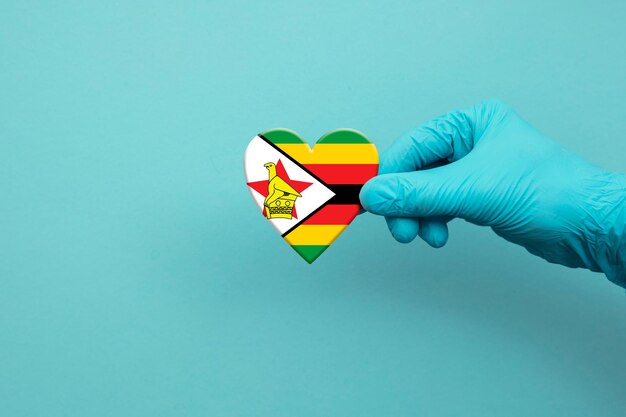 Photo main de travailleurs médicaux portant un gant chirurgical tenant le coeur du drapeau du zimbabwe