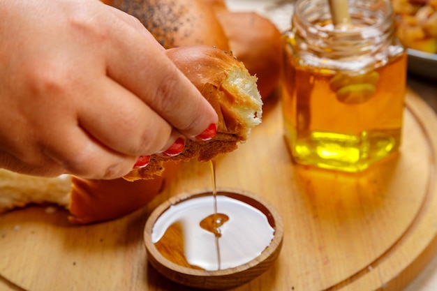 Une main trempe un morceau de challah dans du miel en l'honneur de la célébration de Rosh Hashanah à proximité sur la table du miel et de la challah et de la nourriture traditionnelle