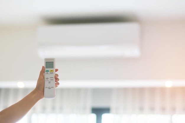 Main utilisant la télécommande pour régler le climatiseur à l'intérieur de la pièce du bureau ou de la maison