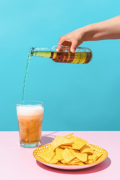 une main versant une bière à côté d'une assiette de nachos sur fond bleu nourriture mexique et été