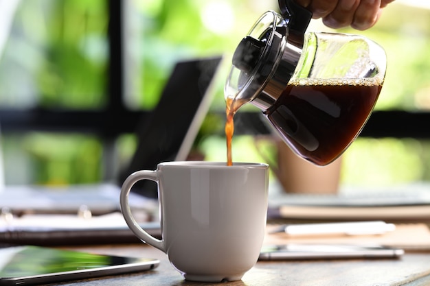 Une main versant du café fumant dans une tasse sur un bureau lorsque vous travaillez à domicile