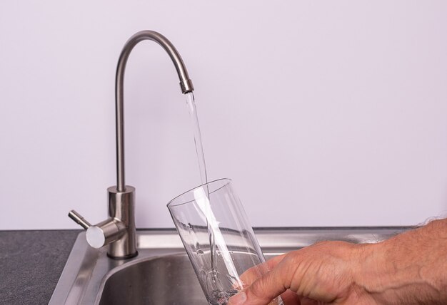 Main versant un verre d'eau du robinet de filtre, mur blanc, espace copie