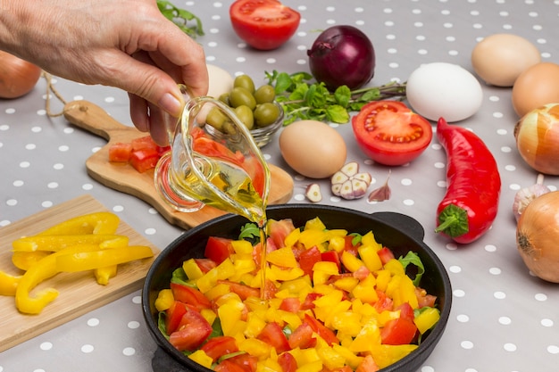 La main verse de l'huile. Tranches de tomates et de légumes verts dans la poêle.