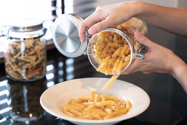 Main verser des pâtes sur un plat blanc dans la cuisine