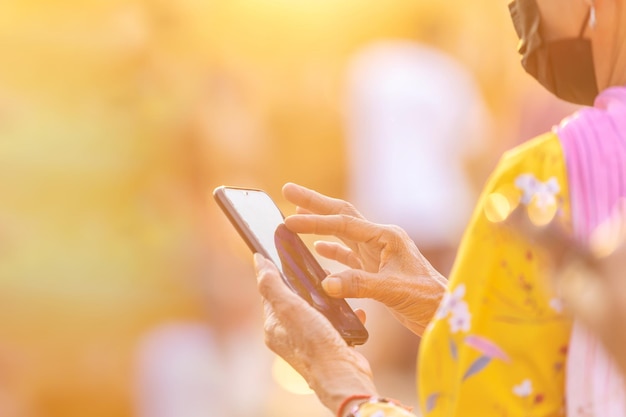 La main d'une vieille femme utilisant un smartphone à l'extérieur le soir