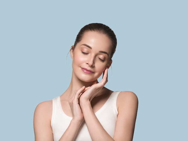 Main de visage de femme en bonne santé de belle peau touchant le fond de couleur de peau fraîche propre et saine. Bleu