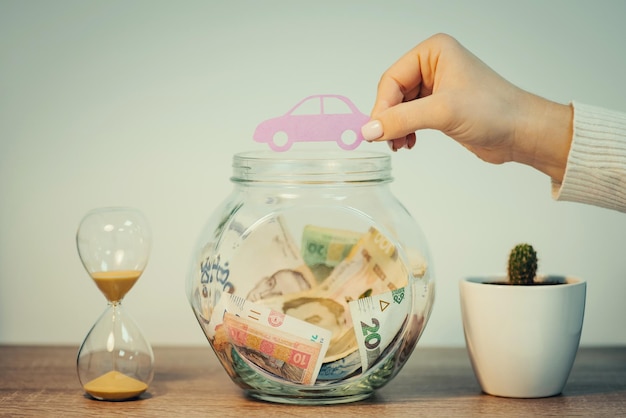 Main avec voiture de symbole de papier près d'un bocal en verre avec des économies de hryvnia Économiser de l'argent pour acheter un nouveau concept de voiture photo aux tons verts