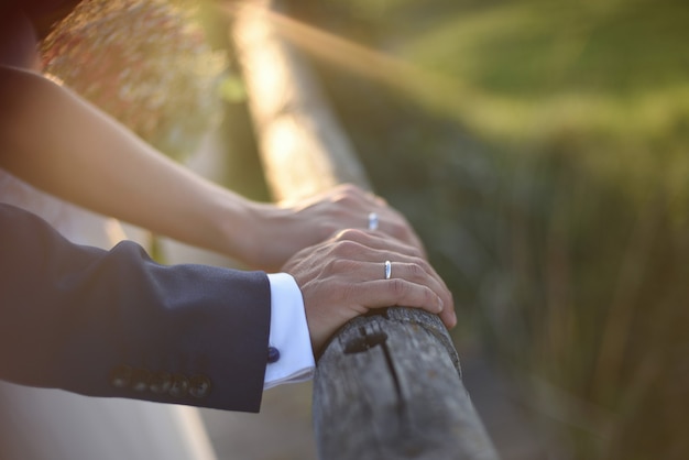 Photo mains avec anneaux de mariage du couple de jeunes mariés au coucher du soleil