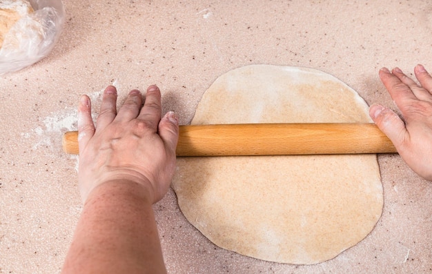 Les mains aplatissent la feuille de pâte à l'aide d'un rouleau à pâtisserie en bois