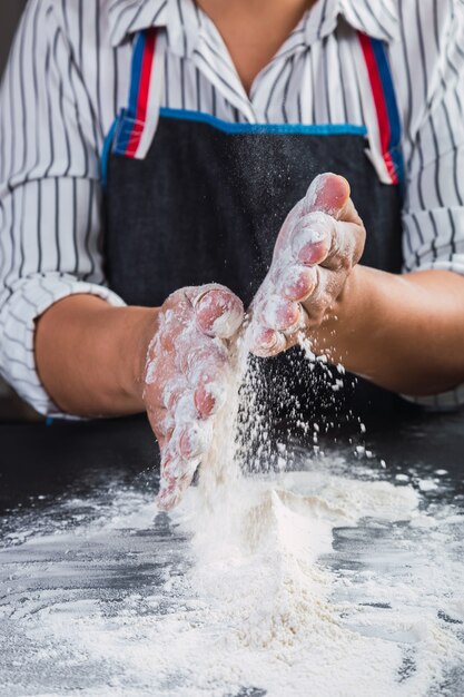 Mains applaudissant et saupoudrant de farine blanche sur la pâte au fond de la cuisine.