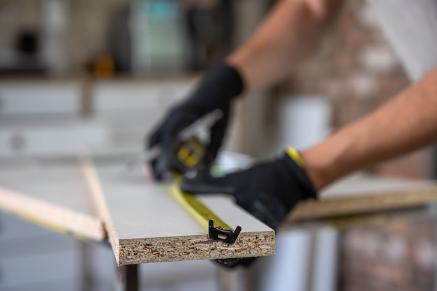 Mains d'artisan utilisant un ruban à mesurer et un crayon pour faire des marques sur un morceau de bois placé.