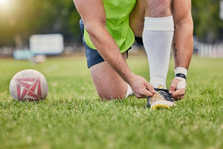 Photo mains de balle de rugby et attacher des lacets de chaussures sur un terrain en herbe se préparant pour un match de sport ou un jeu à l'extérieur