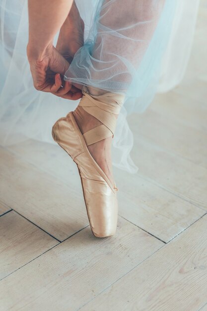 Mains de ballerine en jupe tutu bleu met des chaussures de pointe sur la jambe dans le hall de lumière blanche