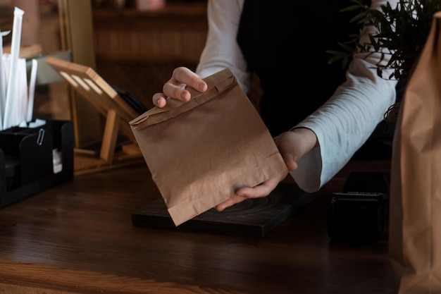 Mains de barista ou vendeur avec sac d'emballage en papier kraft pour emporter de la nourriture