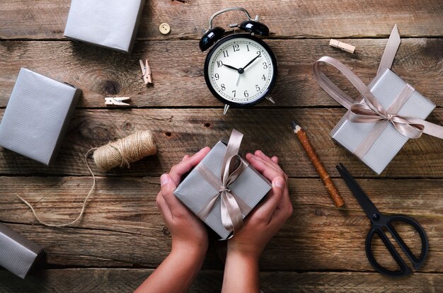 Mains de belle femme tenant une boîte cadeau en bois. Réveil noir, stylo, ciseaux.