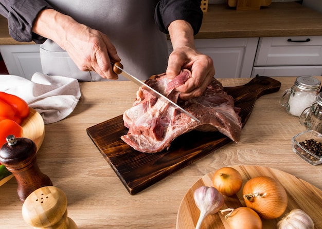 Les mains des bouchers coupent un gros morceau de viande crue sur une planche de bois avec un couteau bien aiguisé le concept de cuisson des aliments à la maison