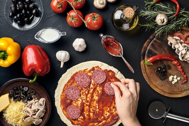 Mains de boulanger ajoutant des ingrédients dans la pizza pendant la préparation de la pizza à la cuisine