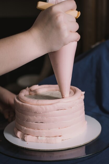 Photo les mains d'une boulangère pressent de la crème rose sur une base de gâteau.