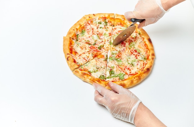 Les mains des boulangers coupent la pizza en morceaux sur un blanc isolé