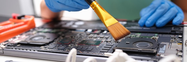 Les mains brossent les pièces de l'ordinateur portable de la poussière avec une brosse