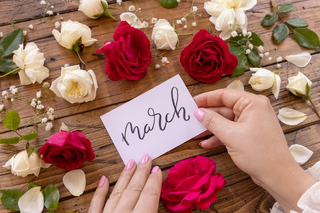 Mains avec carte manuscrite MARS entouré de roses rouges et crème gros plan sur une table en bois Déclaration d'amour romantique féminine près de fleurs Concept de Saint Valentin