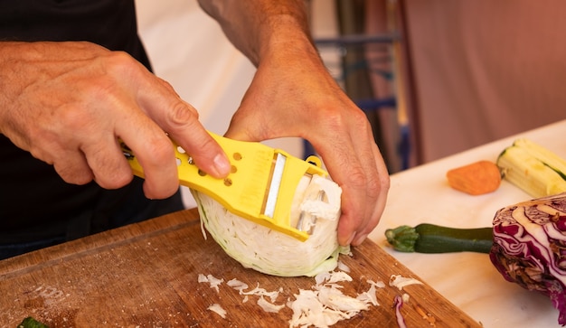 Mains caucasiennes d'un homme coupant des légumes avec un nouvel outil de cuisine. Une seule personne, grand choix de légumes