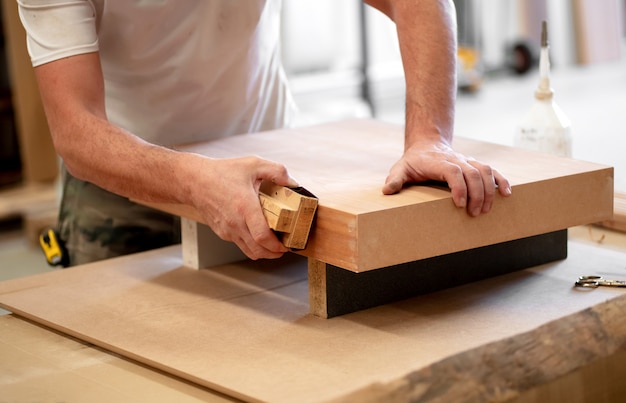 Mains d'un charpentier ponçant le bord d'un bloc