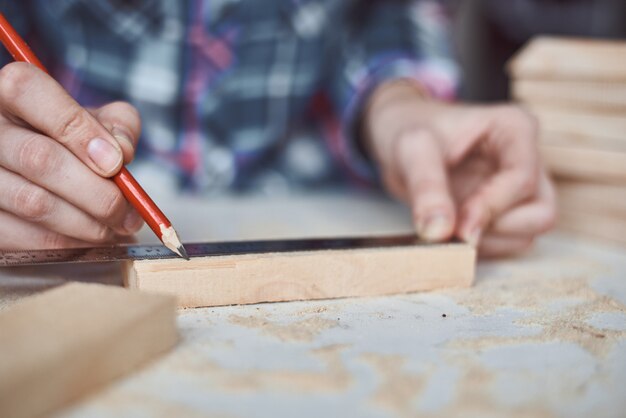 Mains de charpentier prenant la mesure avec un crayon de planche de bois. Concept de menuiserie et de fabrication de meubles