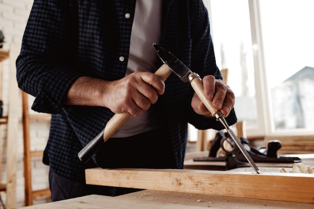 Mains d'un charpentier travaillant avec un burin et un marteau