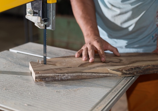 Mains de charpentier travaillant sur une scie à ruban avec une forme en bois pour créer des produits d'intérieur