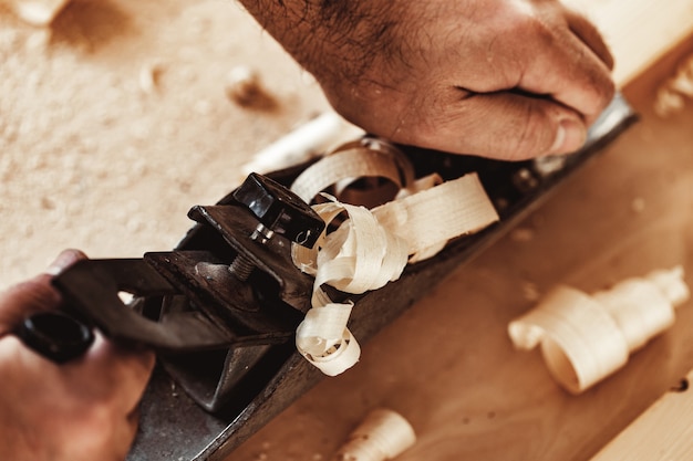 Mains de charpentiers rabotant une planche de bois avec un rabot à main