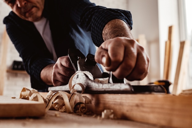 Mains de charpentiers rabotant une planche de bois avec un rabot à main