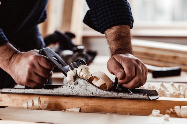 Mains de charpentiers rabotant une planche de bois avec un rabot à main