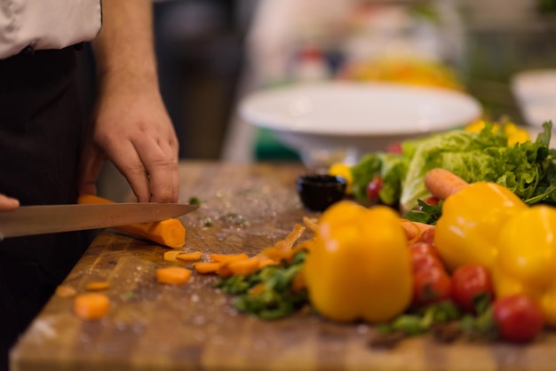 mains de chef coupant des carottes sur une table en bois pour préparer un repas au restaurant