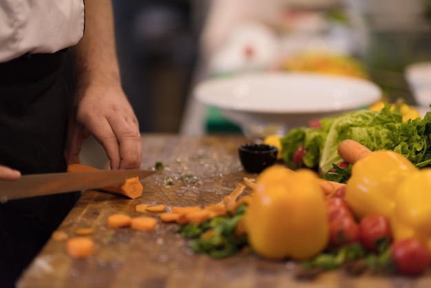 mains de chef coupant des carottes sur une table en bois pour préparer un repas au restaurant