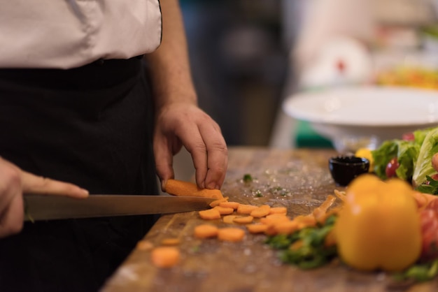 mains de chef coupant des carottes sur une table en bois pour préparer un repas au restaurant