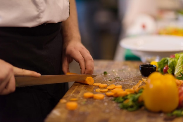 mains de chef coupant des carottes sur une table en bois pour préparer un repas au restaurant