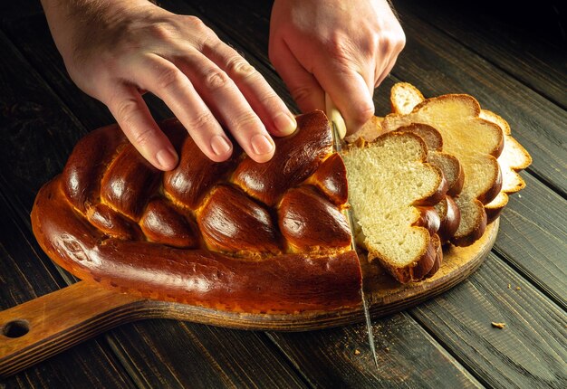 Mains de chef coupées avec un couteau pain frais ou kalach sur une planche à découper de cuisine pour le déjeuner nourriture saine et concept de boulangerie traditionnelle