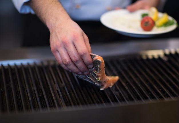 Mains de chef cuisinier faisant cuire du poisson saumon grillé avec des pommes de terre dans une cuisine de restaurant