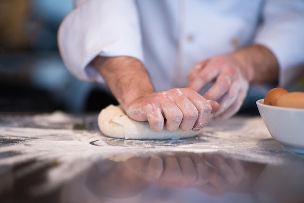 mains de chef préparant la pâte à pizza sur la table saupoudrée de farine gros plan