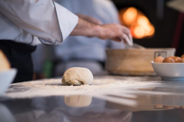 mains de chef préparant la pâte à pizza sur la table saupoudrée de farine gros plan