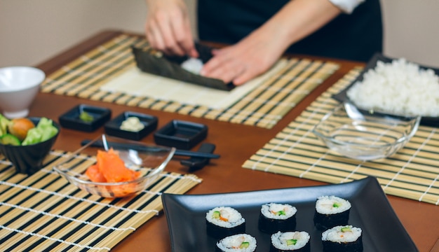 Mains de chef préparant des sushis avec une assiette de rouleaux de maki finis